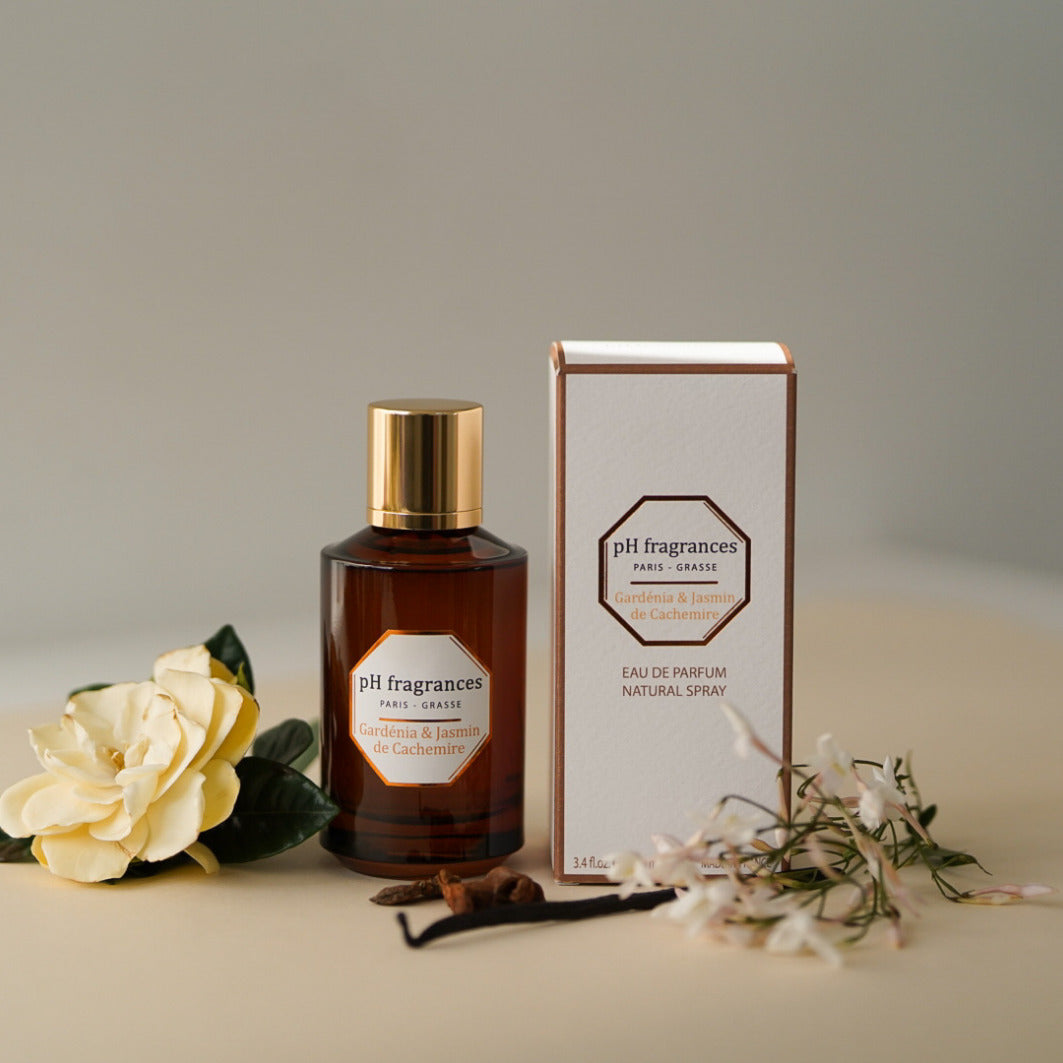 Au centre le flacon de 100ml d'eau de parfum Gardenia Jasmin de Cashmire de la marque pH Fragrances mis en scène avec les éléments qui le composent