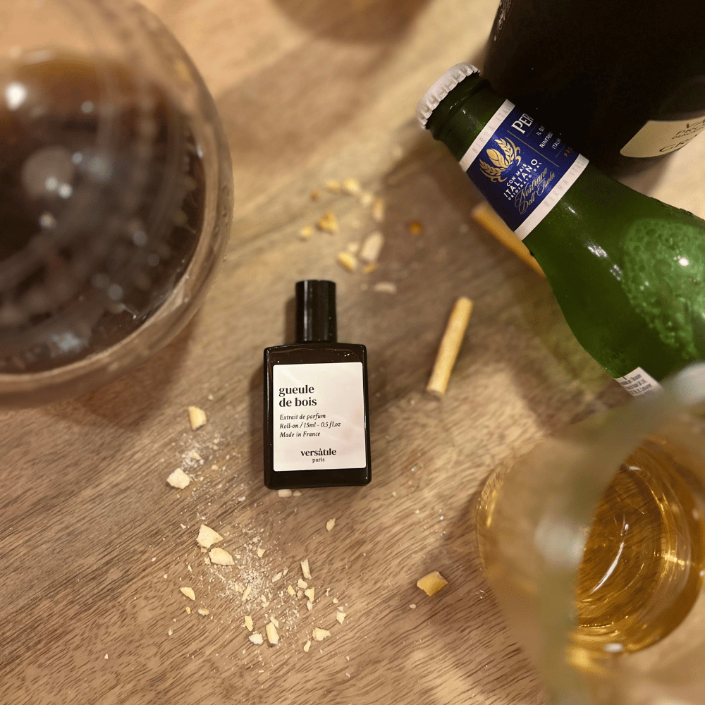 Au centre le flacon de parfum gueule de bois de la marque Versatile entouré des éléments qui composent le parfum : rhum, fond de tabac et bois de santal