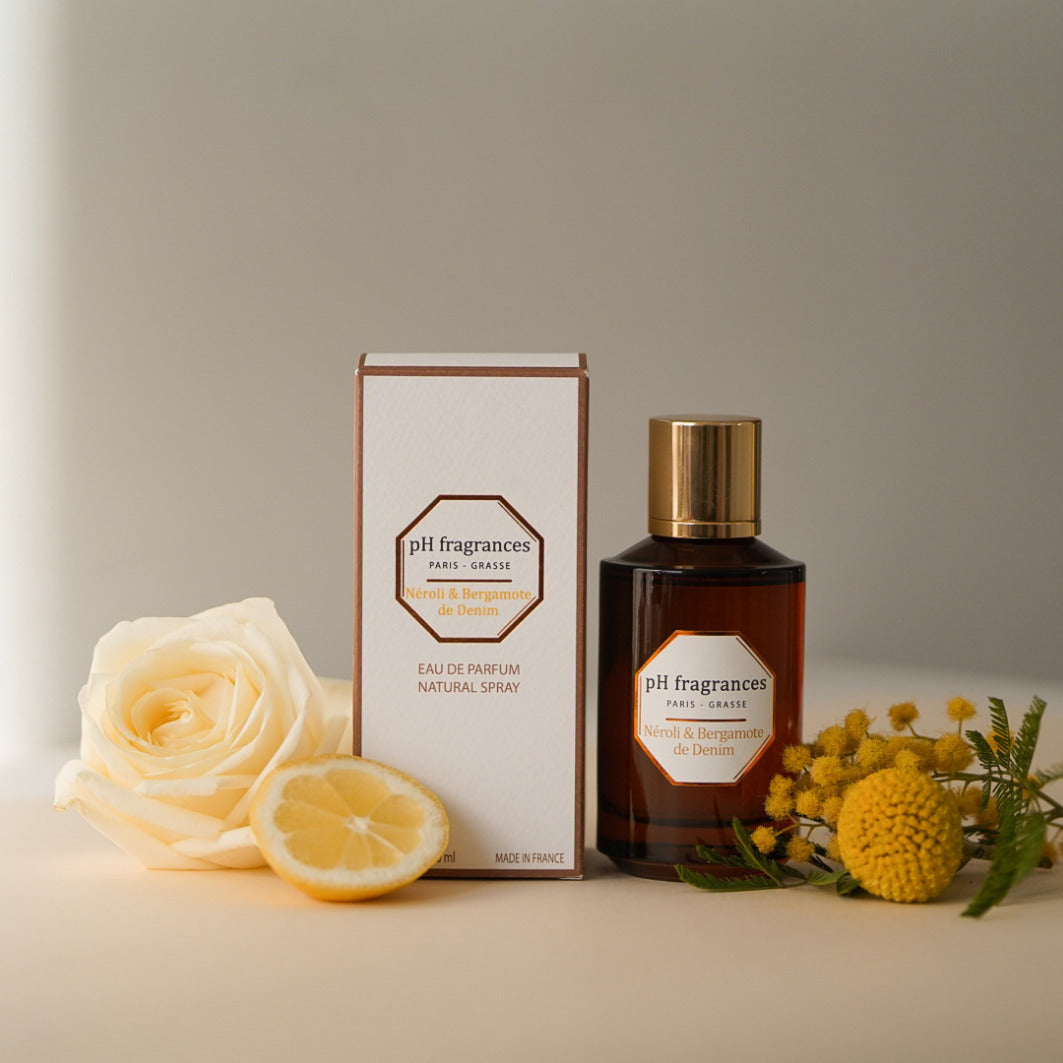 Au centre le flacon de 100ml d'eau de parfum Néroli Bergamote de Denim de la marque pH Fragrances mis en scène avec les éléments qui le composent