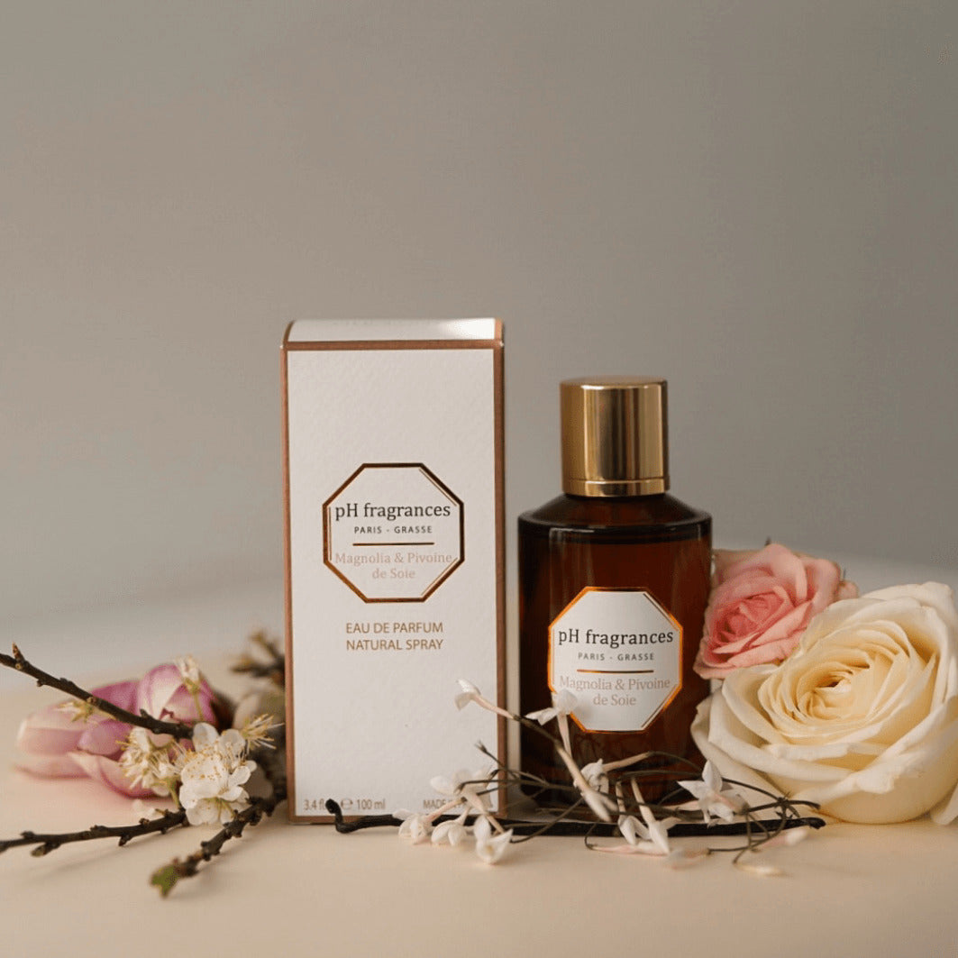 Au centre le flacon de Magnolia & Pivoine de Soie de la marque pH Fragrances entouré des éléments qui le composent : pivoine, rose, vanille et fleur d'oranger. 