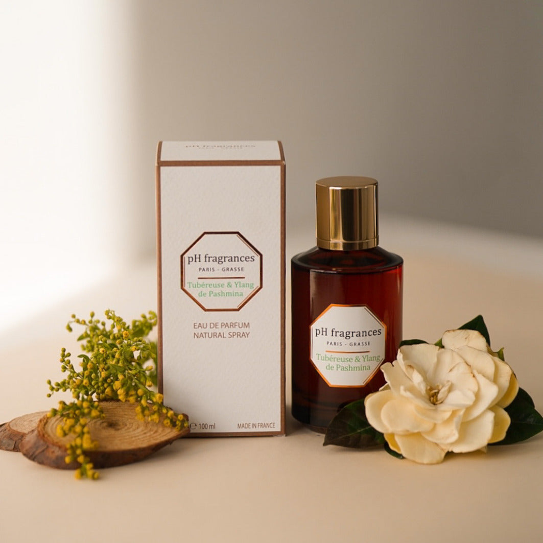 Au centre le flacon de 100ml d'eau de parfum Vetiver & Santal de Cuir de la marque pH Fragrances mis en scène avec les éléments qui le composent : mimosa, tubéreuse